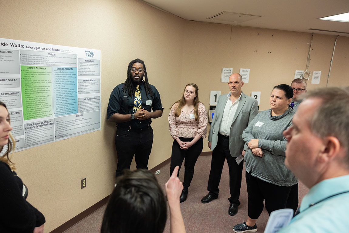 A group of college students and adults gather around a poster about segregation (also known as solitary confinement) and have a discussion